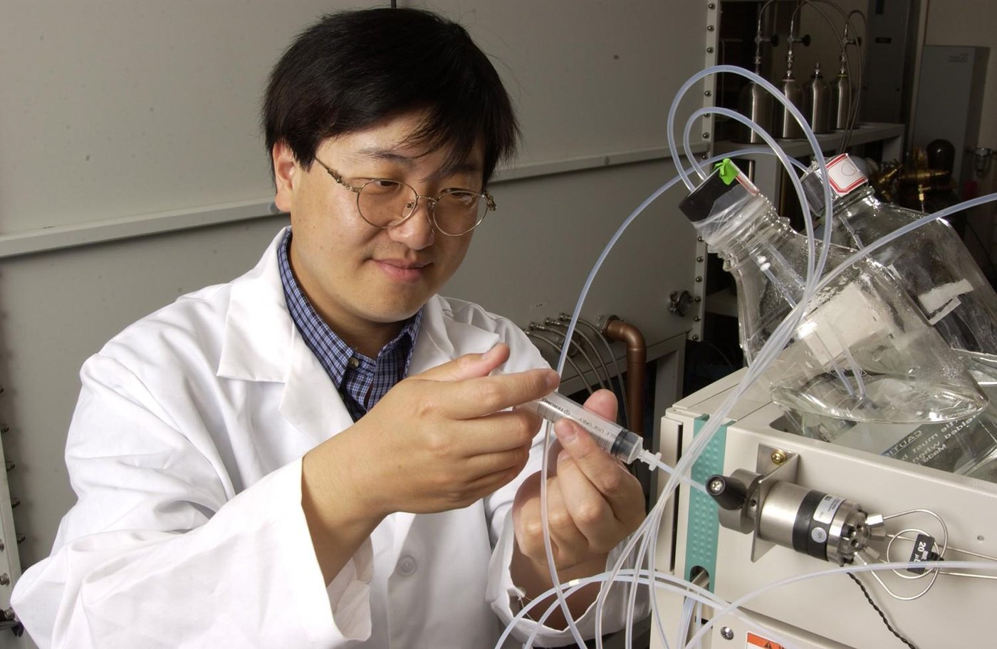 A research chemist handling newly synthesized products at the bench (Ames Laboratory, U.S. DOE) — the craft behind custom peptide manufacturing; a ChemBioSyn capability brief by Panacea Bio Chem and Bogdan Dicoias